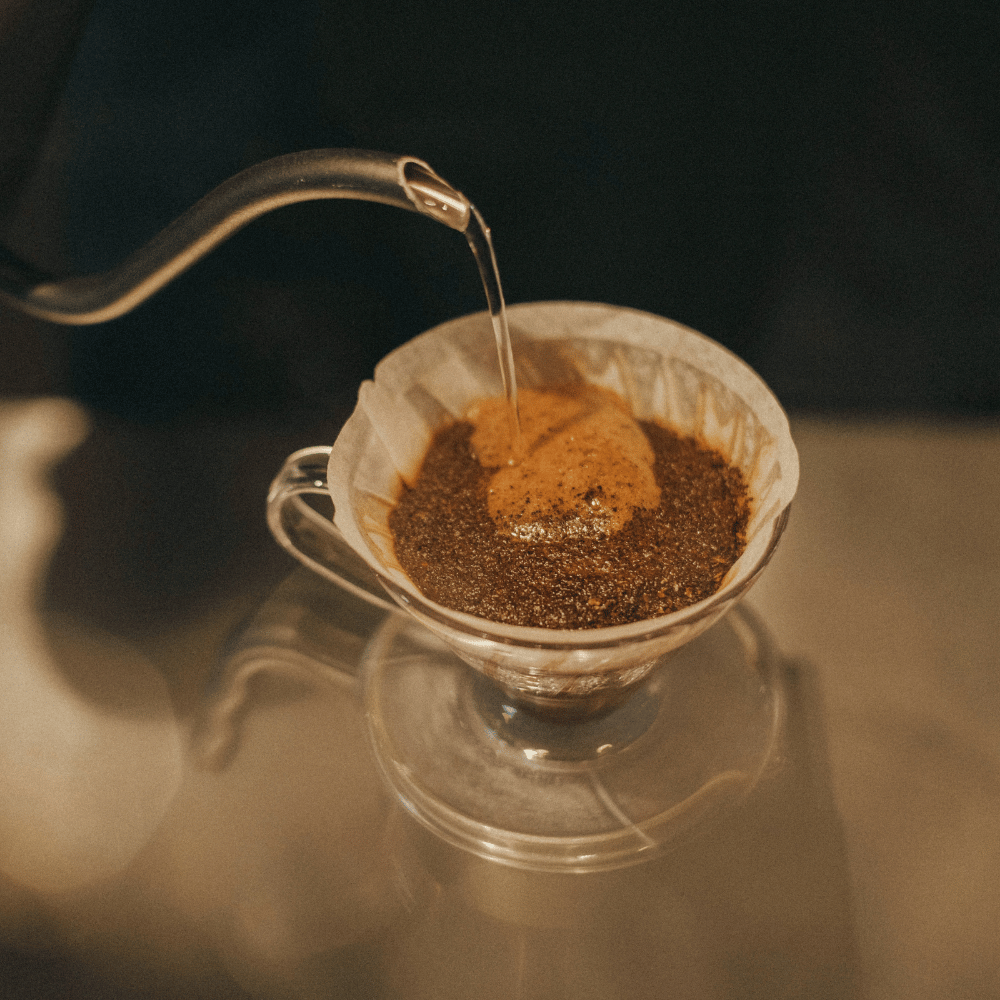 Vand hældes fra en gooseneck-kedel over friskkværnet kaffe i en V60 pour over-brygger med papirfilter under brygning.